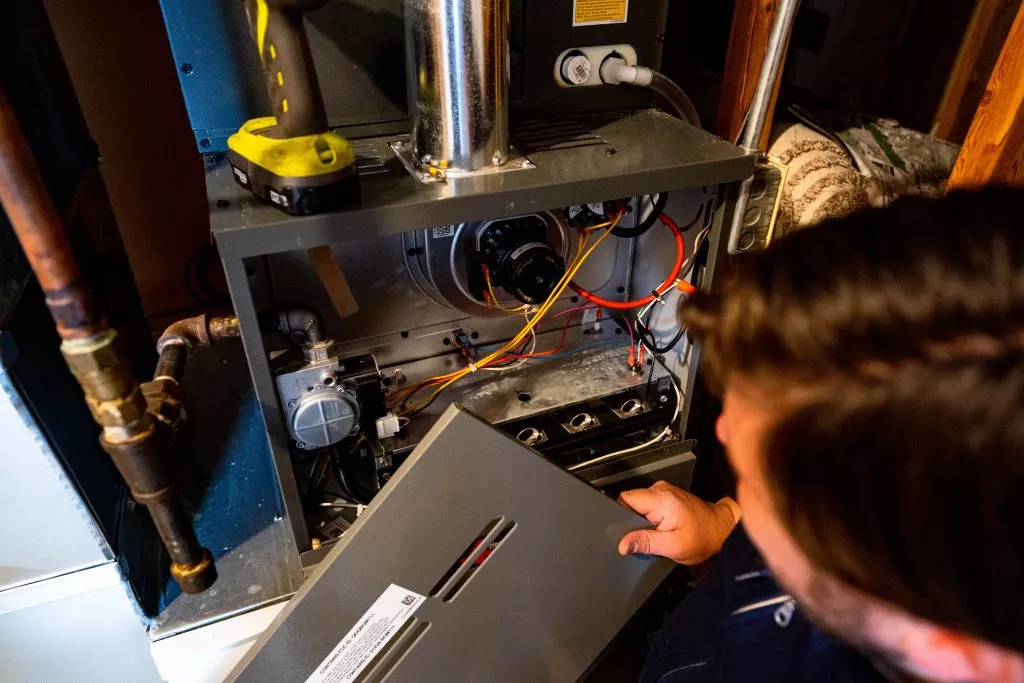 Technician examining the interior of a furnace during maintenance, showcasing wires and components for optimal heating system performance.