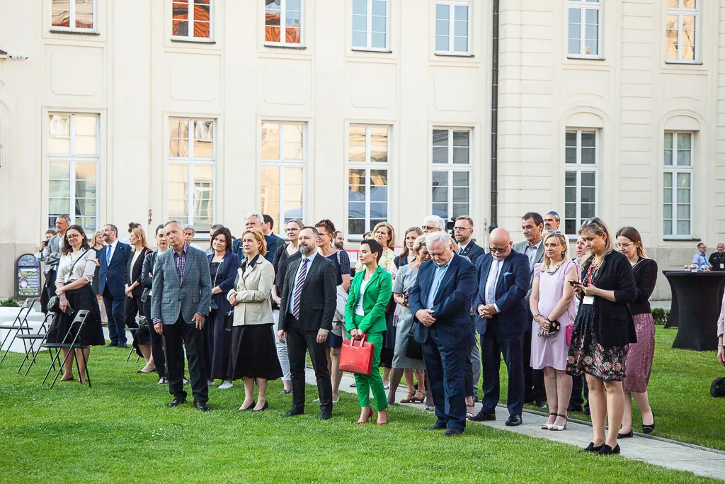 Publiczność stoi na porośniętym trawą dziedzińcu Ministerstwa Kultury, Dziedzictwa Narodowego i Sportu.