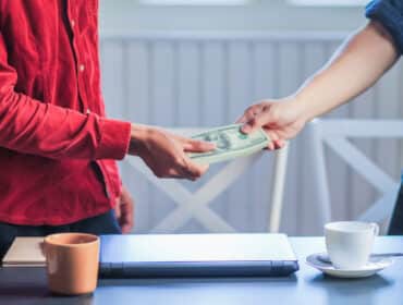 Deux individus échangeant de l'argent autour d'une table avec un ordinateur portable et des tasses à café, soulignant le devoir de secours entre époux.