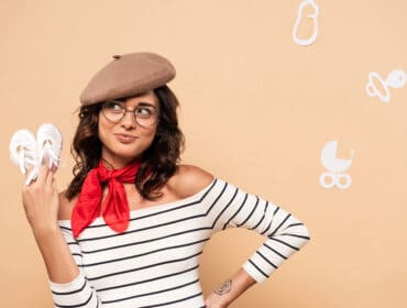 pregnant french woman in beret holding shoes on beige background