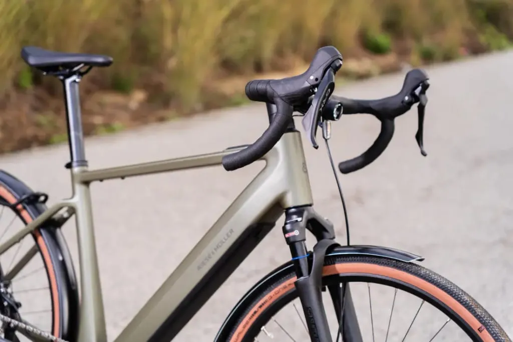 Primer plano de una bicicleta Riese & Müller UBN Five en la carretera, con un cuadro elegante, manillar bajo y llamativos neumáticos negros con marrones.
