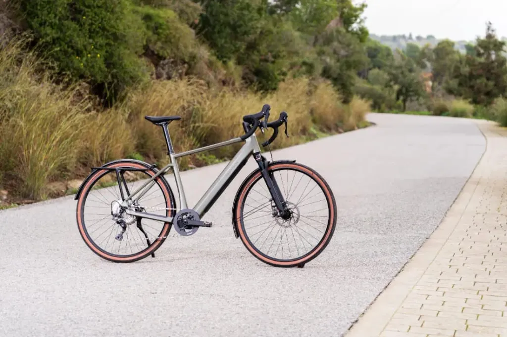 Una elegante bicicleta de ruta, como la versátil UBN Five Commute, se desliza por un camino pintoresco y sinuoso rodeado de exuberante vegetación.