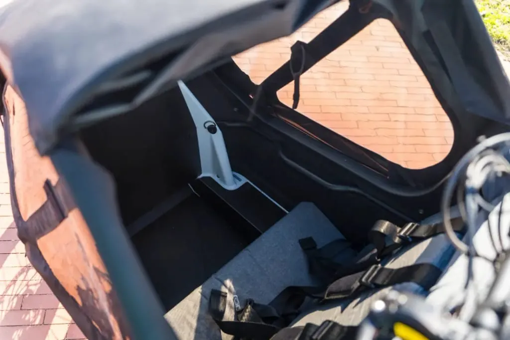 El interior de un remolque para bicicletas cubierto, diseñado para familias urbanas, cuenta con asientos y cinturones de seguridad y está estacionado sobre una superficie de ladrillo. Perfectamente compatible con la bicicleta de carga eléctrica Riese & Müller Packster2 70 CT Vario.