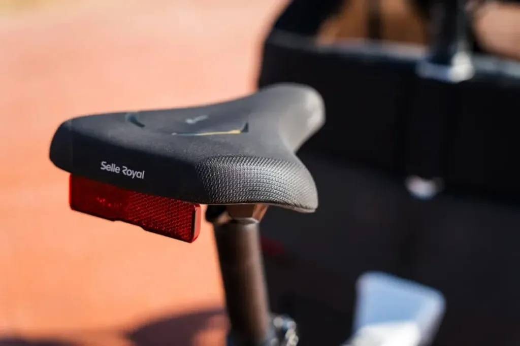 Primer plano de un sillín de bicicleta con un reflector rojo colocado, tomando el sol. Este elegante detalle es parte de la Riese & Müller Packster2 70 CT Vario, una bicicleta de carga eléctrica diseñada perfectamente para familias urbanas que se desplazan por la vida urbana.