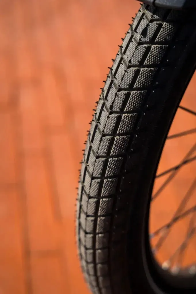 Primer plano de una cubierta de bicicleta Riese & Müller Packster2 70 CT Vario con dibujo texturizado, sobre un fondo de ladrillo rojizo difuminado. Perfecta para familias urbanas que buscan una bicicleta de carga eléctrica que combine estilo y funcionalidad.