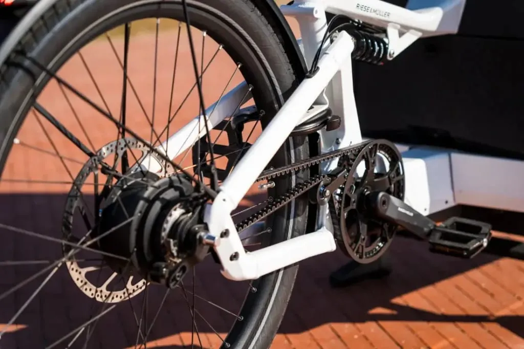 Primer plano de la rueda trasera y los engranajes de una bicicleta Riese & Müller, que muestra el freno de disco y el mecanismo de cadena en un día soleado, perfecto para familias urbanas que navegan en aventuras en bicicletas de carga eléctricas.