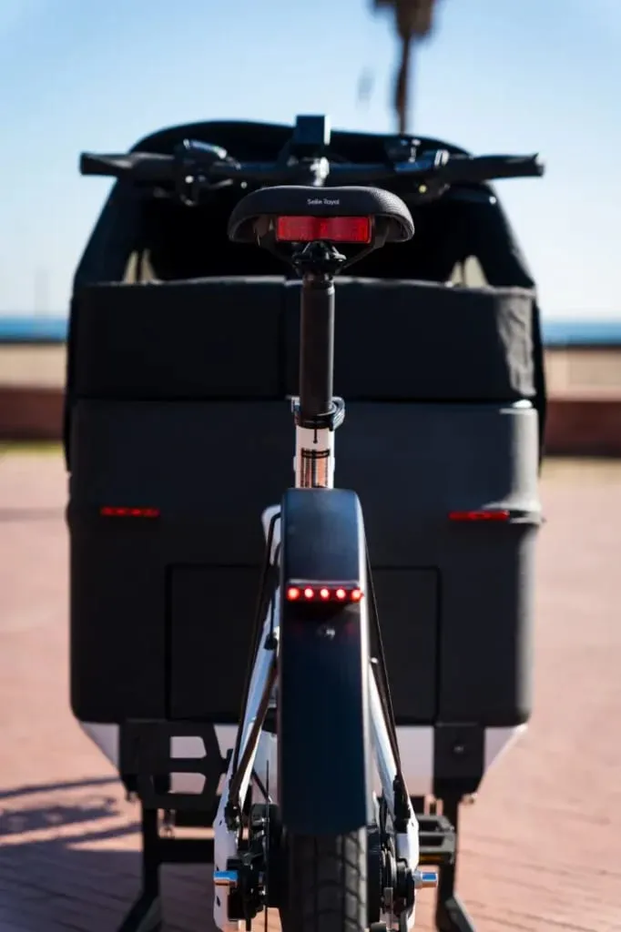 Vista trasera de la Packster2 70 CT Vario, una bicicleta de carga eléctrica con un compartimento de almacenamiento negro, perfecta para familias urbanas que recorren la ciudad en un día soleado.