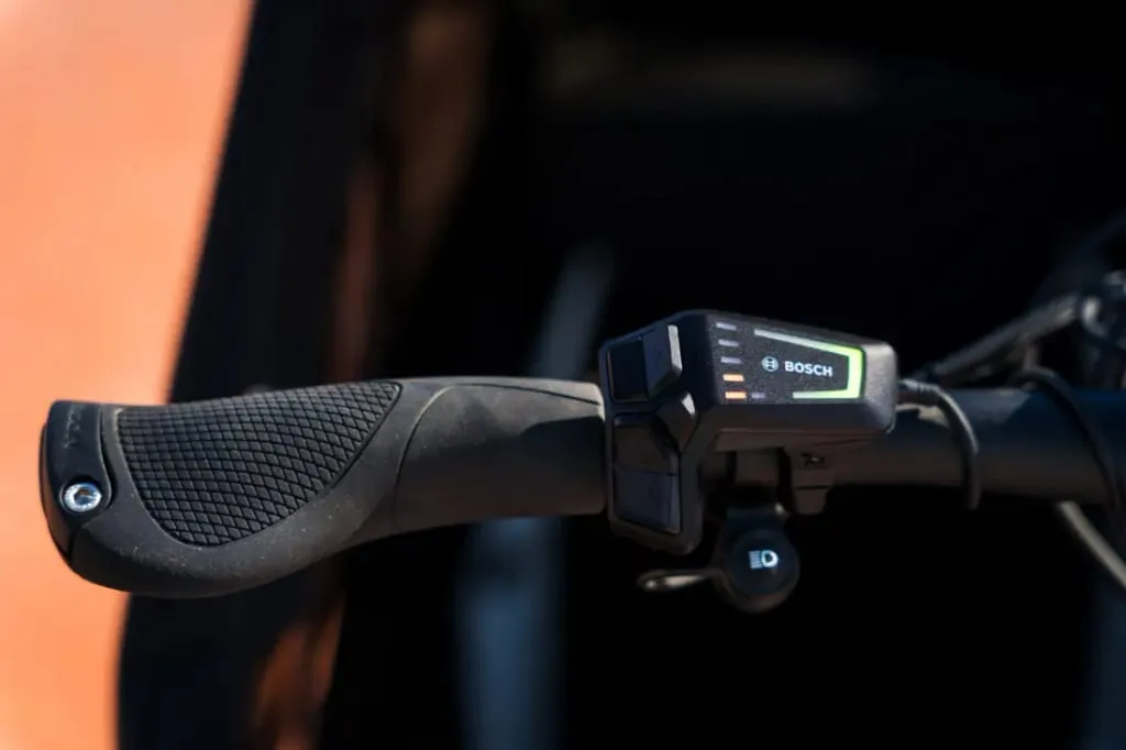 Primer plano de un manillar de bicicleta con un panel de control electrónico de Bosch que muestra indicadores de nivel de batería en la Riese & Müller Packster2 70 CT Vario, perfecta para familias urbanas que buscan una bicicleta de carga eléctrica eficiente.