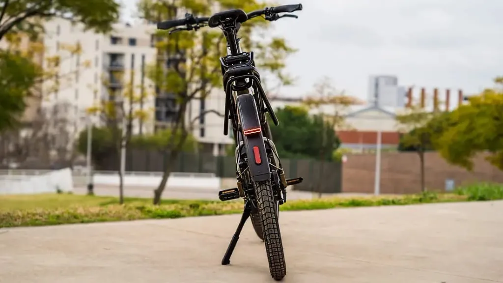 Una bicicleta eléctrica urbana está estacionada en un camino, rodeada de árboles y edificios, ofreciendo una mezcla perfecta de comodidad y tecnología de vanguardia.