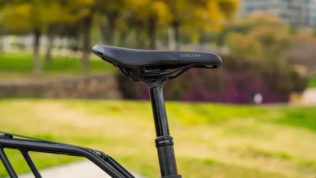 Primer plano del asiento y el poste de una bicicleta, que muestra la tecnología de vanguardia de una bicicleta eléctrica urbana, con un paisaje de parque borroso en el fondo.
