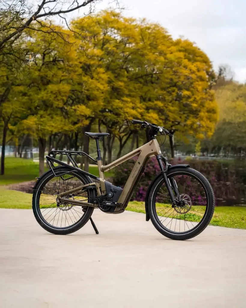 Una bicicleta eléctrica urbana descansa sobre un camino pavimentado en el parque, enmarcada por árboles de hojas amarillas, ofreciendo tanto comodidad como un toque de tecnología de vanguardia.