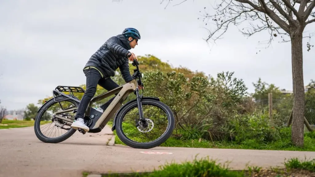 Una persona con casco viaja cómodamente en una bicicleta eléctrica urbana por un sendero rodeado de exuberante vegetación, disfrutando de la tranquilidad y la tecnología de punta que mejora cada recorrido.