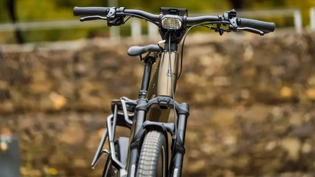 Vista frontal de una elegante bicicleta eléctrica Riese & Müller con neumáticos gruesos, que muestra su tecnología de vanguardia, estacionada al aire libre contra un fondo natural bellamente borroso.