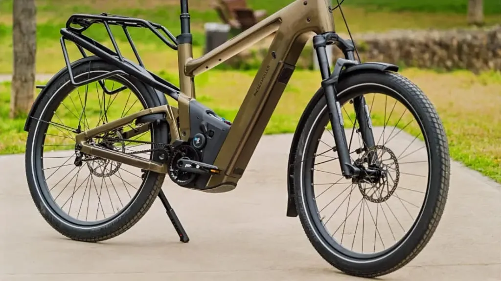 Primer plano de una bicicleta eléctrica urbana con cuadro negro y oliva, que muestra tecnología de vanguardia, estacionada en un camino de concreto en una zona verde.