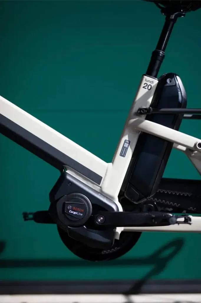 Primer plano del cuadro de una bicicleta eléctrica Moustache Lundi 20 Cargo, resaltando el motor y la batería Bosch sobre un fondo verde.