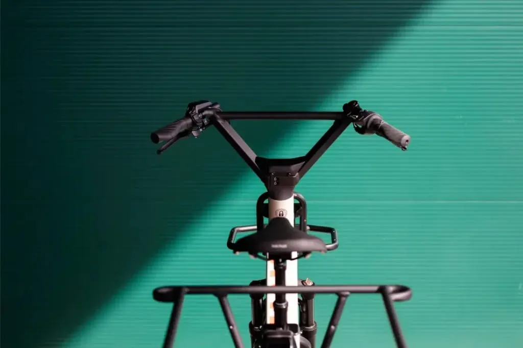 Manillar y asiento de bicicleta de carga Moustache Lundi 20 sobre un fondo verde azulado con una sombra diagonal.