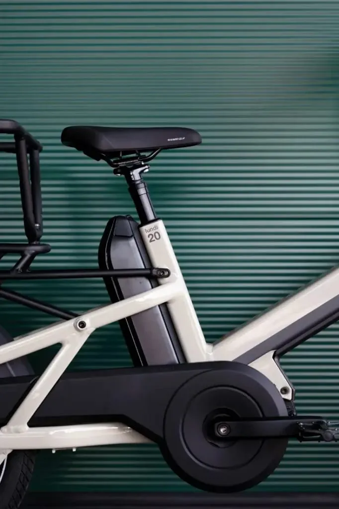 Primer plano del cuadro, la batería y el asiento de una bicicleta eléctrica Moustache Lundi 20 Cargo sobre un fondo acanalado verde.