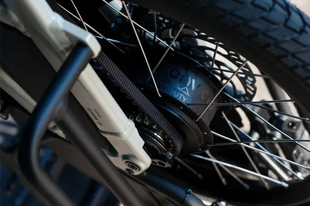 Primer plano de la rueda trasera de una bicicleta Moustache Lundi 20 Cargo, resaltando el buje, los radios, el neumático y el innovador sistema de transmisión por correa.
