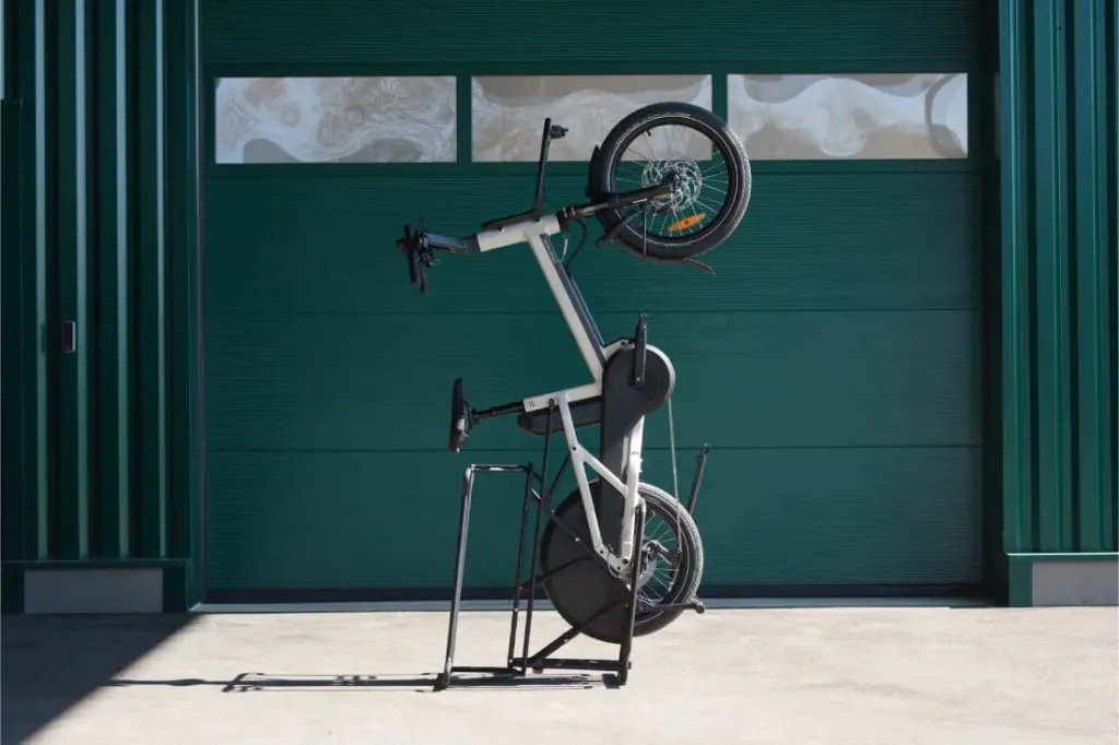 Una bicicleta de carga Moustache Lundi 20 se encuentra verticalmente sobre su rueda trasera frente a una gran puerta de garaje verde.
