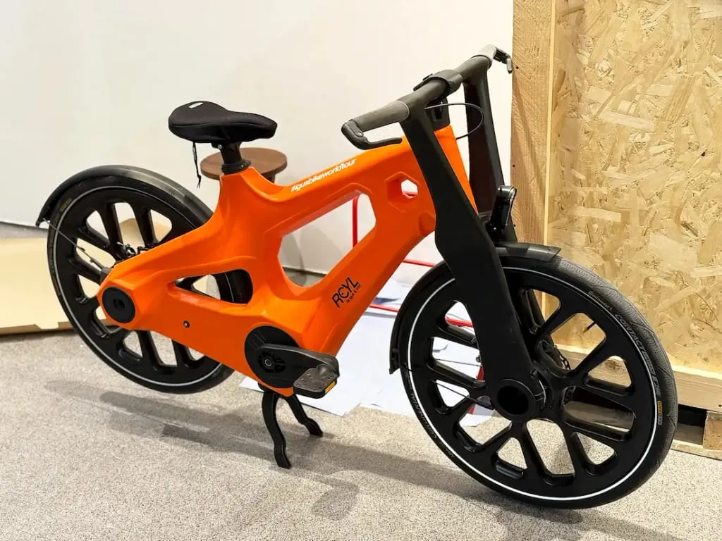Bicicleta futurista de igus de color naranja brillante con un marco sólido único, ruedas negras y sin cadena ni engranajes visibles, perfecta para la movilidad urbana.