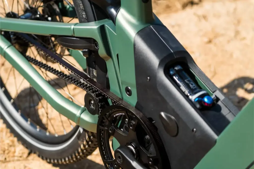 Primer plano del cuadro, el motor y el sistema de transmisión por correa Rohloff de una bicicleta eléctrica Riese & Müller Superdelite5 GT, con suelo arenoso al fondo.
