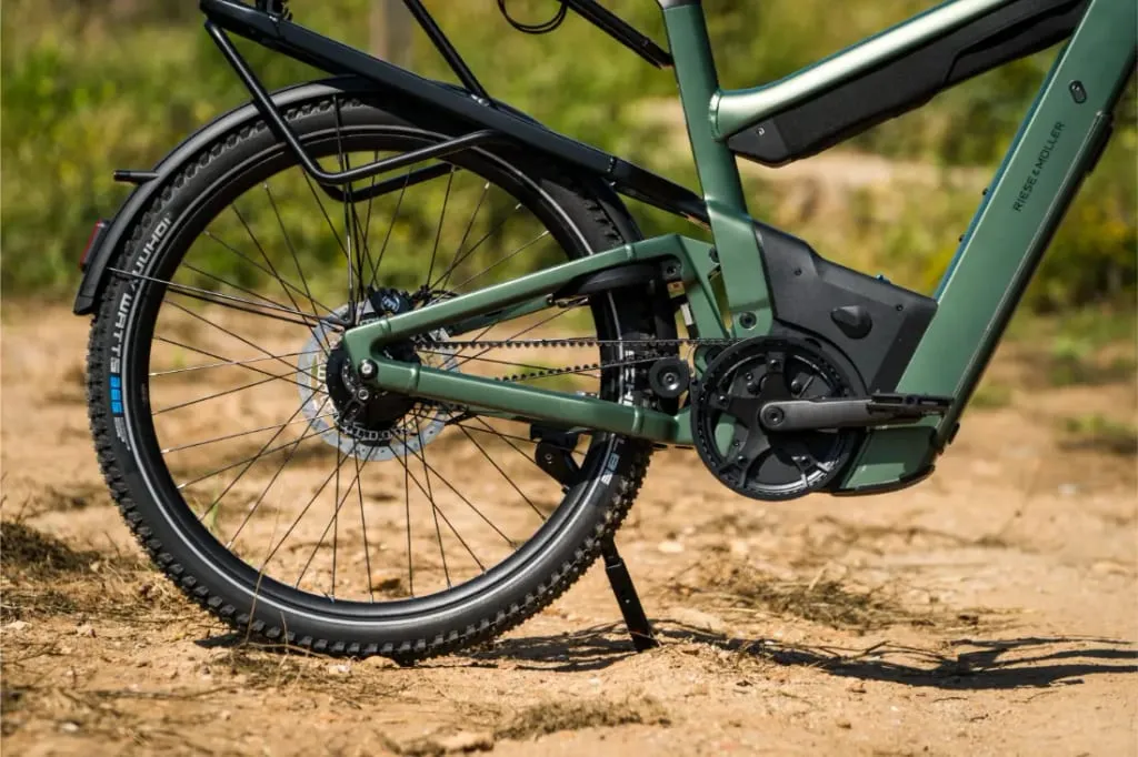 Primer plano de la rueda trasera y la zona de los pedales de una bicicleta eléctrica Riese & Müller Superdelite5 GT rohloff verde en un camino de tierra.