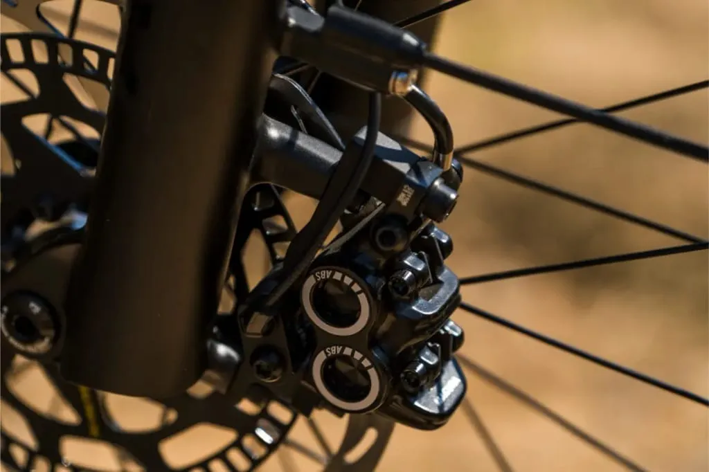 Primer plano de una pinza de freno de disco y un rotor de bicicleta Riese & Müller Superdelite5 GT rohloff con radios al fondo, lista para cualquier aventura.