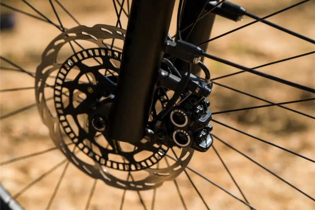 Primer plano del freno de disco y el rotor de una bicicleta Riese & Müller Superdelite5 GT montados en la rueda delantera, con un fondo borroso.