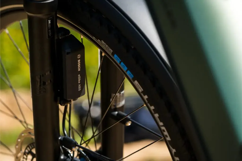 Primer plano de una rueda delantera de bicicleta Superdelite5 GT de Riese & Müller, con un sensor ABS de Bosch colocado cerca del neumático y la horquilla, y equipada con un buje de cambio Rohloff.