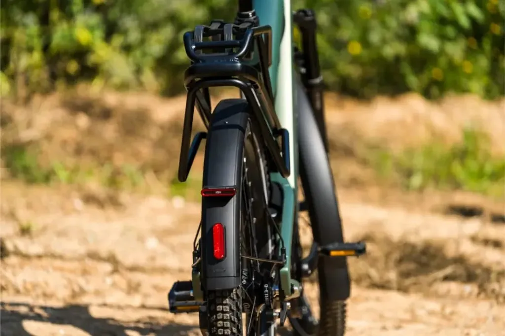 Primer plano de la rueda trasera, el guardabarros y el portaequipaje de una Riese & Müller Superdelite5 GT Rohloff en un camino de tierra, perfecto para la aventura, con una exuberante vegetación de fondo.