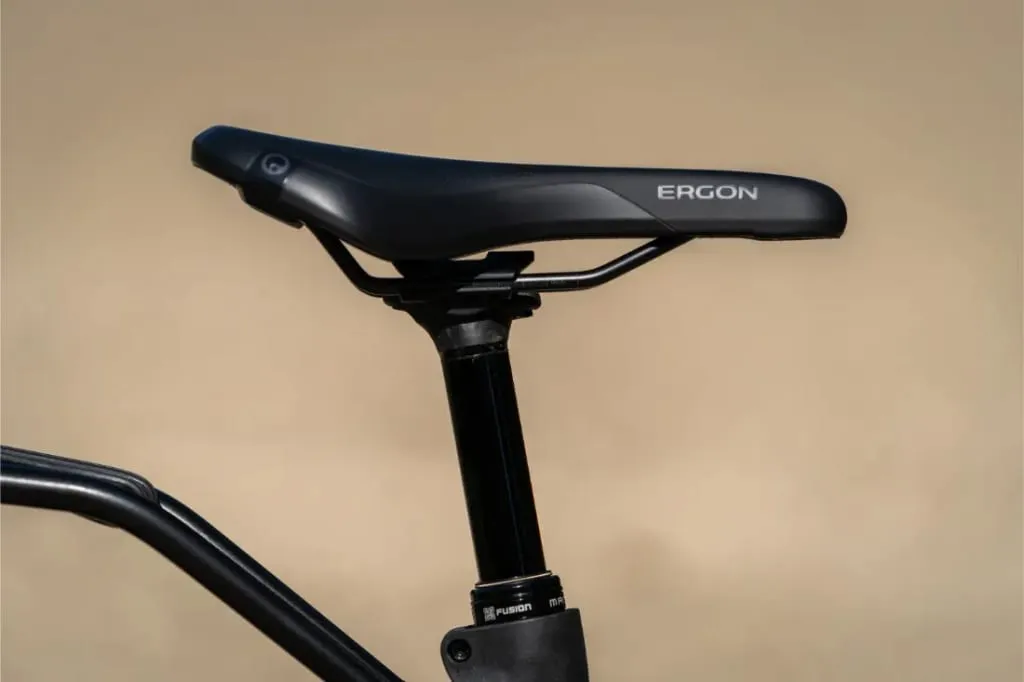 Primer plano de un sillín de bicicleta Ergon negro sobre una tija de sillín Riese & Müller Homage5 GT con cuadro de paso bajo, sobre un fondo liso.