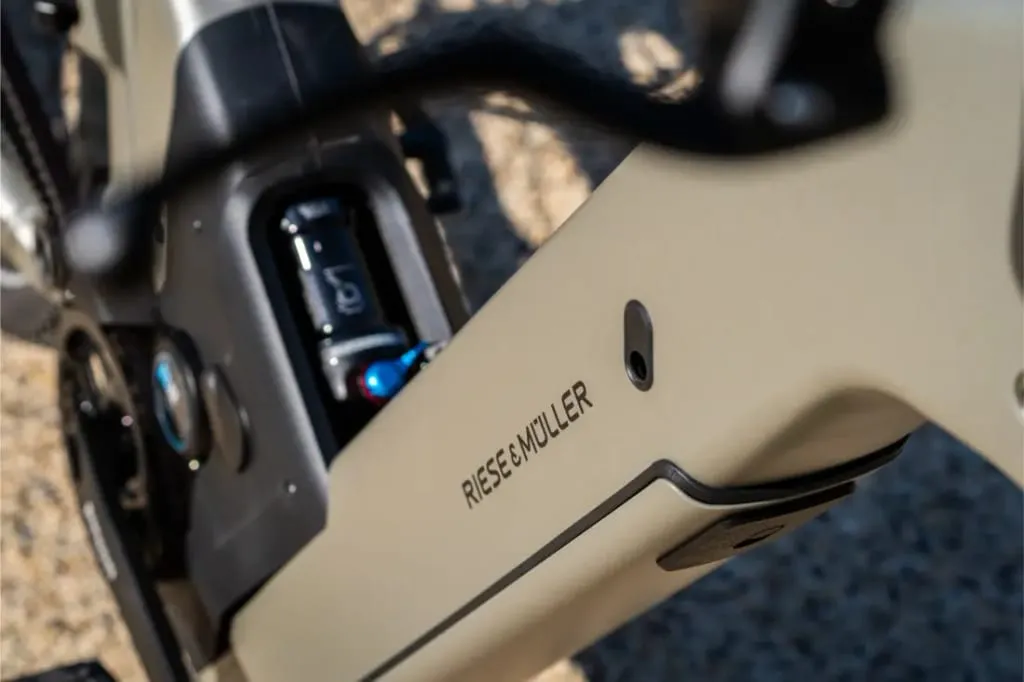 Primer plano del cuadro de una bicicleta eléctrica Riese & Müller Homage5 con diseño de paso bajo, en el que destaca el logotipo de la marca y los componentes de la suspensión.