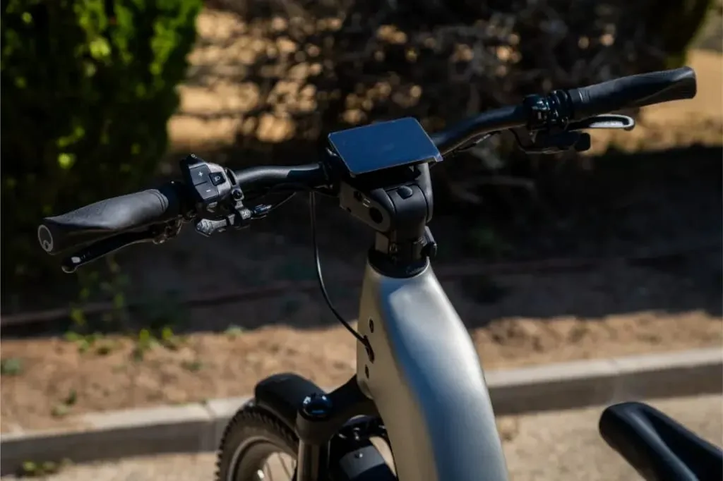 Primer plano de un manillar de bicicleta eléctrica Homage5 GT de Riese & Müller con una pantalla de visualización montada, con un sistema de engranaje de piñón, al aire libre bajo la luz del sol.