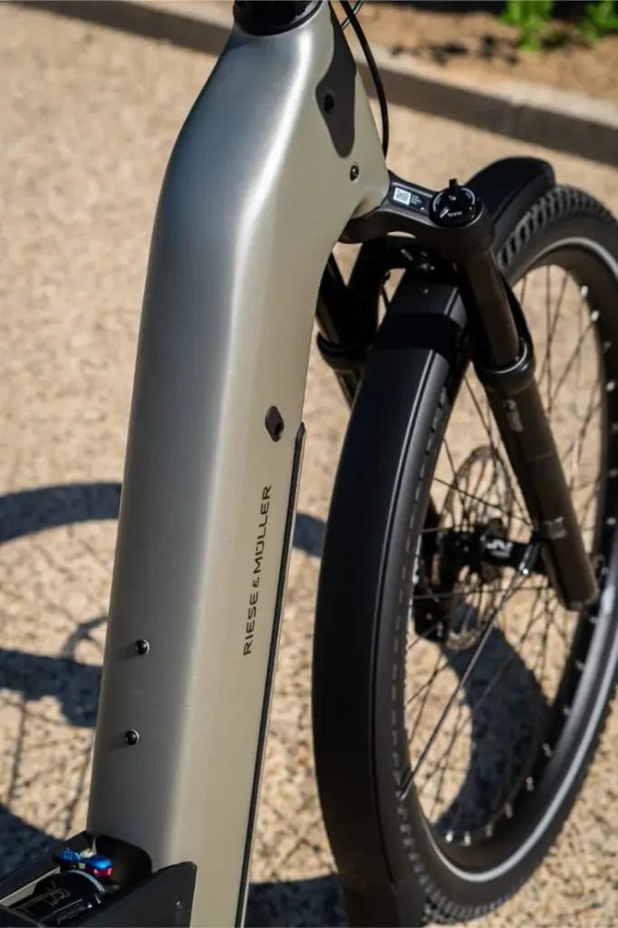 Primer plano del cuadro y la rueda delantera de una bicicleta eléctrica de piñón Riese & Müller Homage5 GT con diseño de paso bajo en un camino de grava.