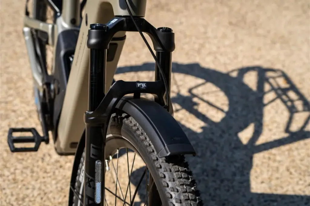 Primer plano de la rueda delantera, el neumático y el guardabarros de una bicicleta Riese & Müller Homage5 con su sombra sobre una superficie de grava, con el piñón GT y el diseño de paso bajo.