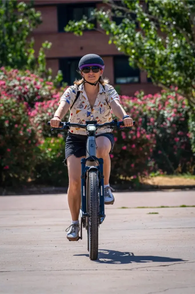 Persona con gorra y gafas de sol monta en una bicicleta Riese & Müller Homage5 al aire libre en un día soleado, con vegetación de fondo.