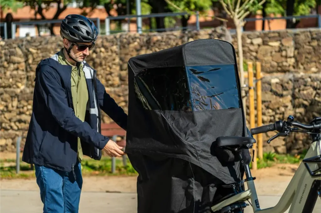Hombre con casco cerrando la cremallera del compartimento de carga de un remolque Riese & Müller Multicharger3 Mixte Vario al aire libre en un día soleado.