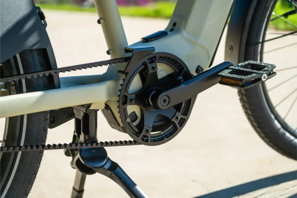 Primer plano de las bielas, el pedal, la transmisión por correa y la pata de cabra de una Riese & Müller Multicharger3 Mixte Vario e-bike en un día soleado, lista para manejar cualquier carga con facilidad.