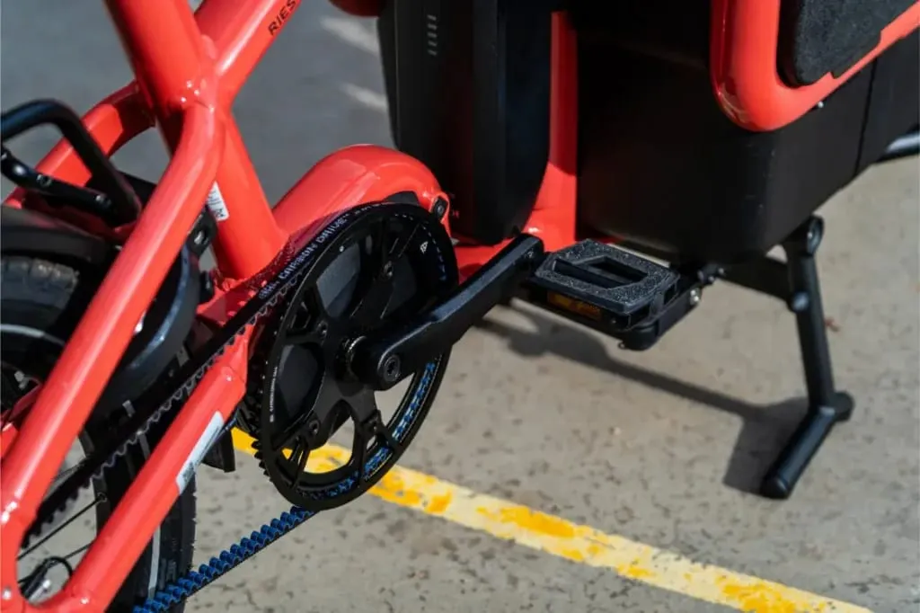 Primer plano del pedal, la biela y el plato de una bicicleta Riese Müller roja -que muestra su tamaño compacto- aparcada en una superficie de hormigón con líneas amarillas.