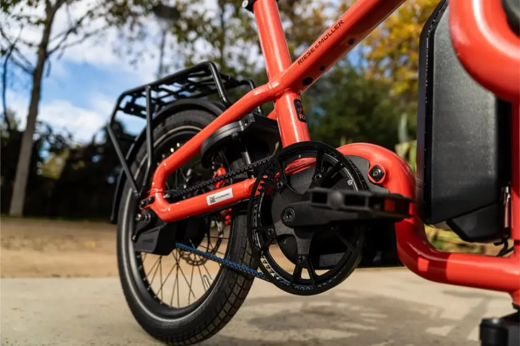 Primer plano del cuadro compacto, la rueda trasera y el sistema de cambios de una bicicleta eléctrica automática Riese Müller Carrie2 roja al aire libre.
