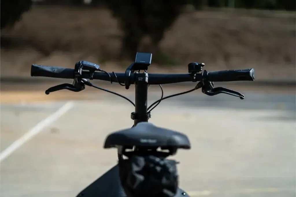Primer plano del manillar y el sillín de la bicicleta Riese Müller Carrie2, mostrando su tamaño compacto y sus funciones automáticas sobre un fondo borroso al aire libre.