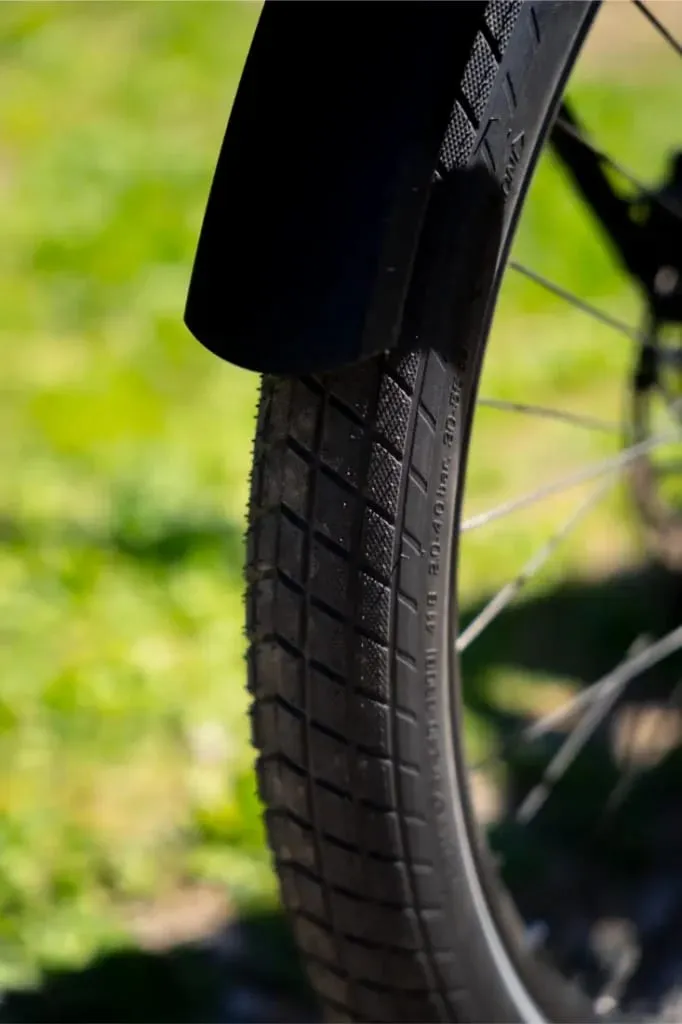Primer plano de un neumático de bicicleta Riese & Müller Nevo5 con dibujo de la banda de rodadura, al aire libre en un día soleado con hierba verde de fondo: donde el lujo accesible se une al rendimiento.