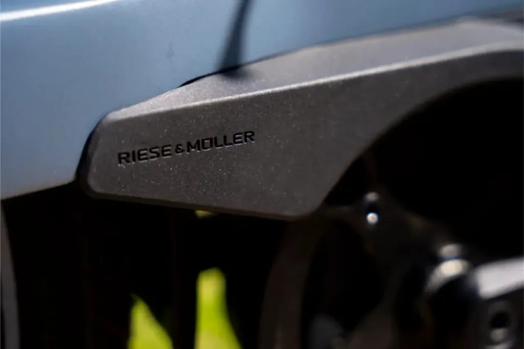 Primer plano de un cuadro negro de bicicleta Riese & Müller Nevo5 con el logotipo "Riese & Müller", parte de la rueda visible a la derecha, que muestra la silenciosa tecnología CORE y un toque de lujo en su elegante diseño.