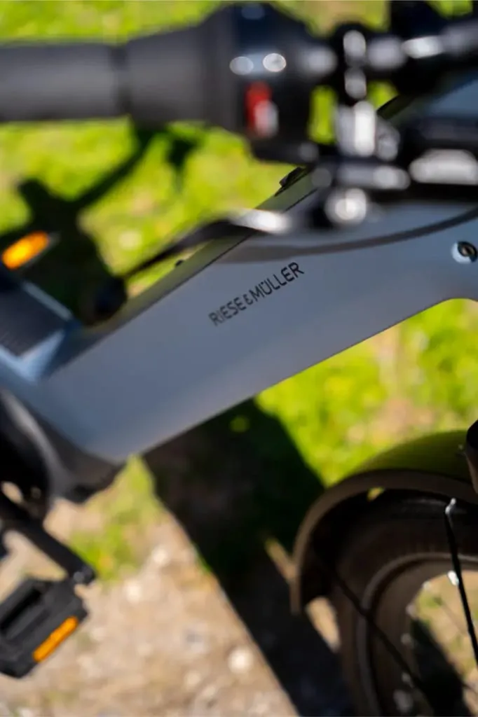Primer plano del cuadro de la bicicleta Nevo5 de Riese & Müller con manillar y pedales, al aire libre en un día soleado, mostrando un diseño accesible e innovador.