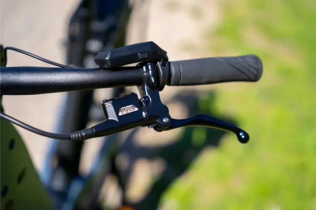 Primer plano de un manillar de bicicleta Nevo5 de Riese & Müller con una palanca de freno y un pequeño dispositivo electrónico, en el que destaca la integración de lujo accesible y silenciosa de CORE.