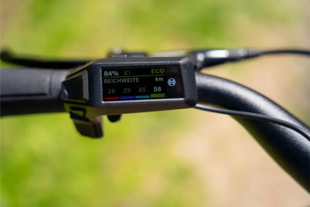 Detalle de la pantalla del manillar de una e-bike Nevo5 de Riese & Müller que muestra el nivel de batería, la velocidad y la autonomía en kilómetros para una experiencia de lujo accesible.