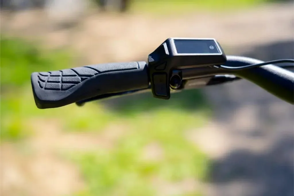 Primer plano de un puño negro de manillar de bicicleta con pantalla electrónica, a la luz del sol, en el Nevo5 de Riese & Müller, una mezcla perfecta de tecnología CORE silenciosa y lujo accesible.