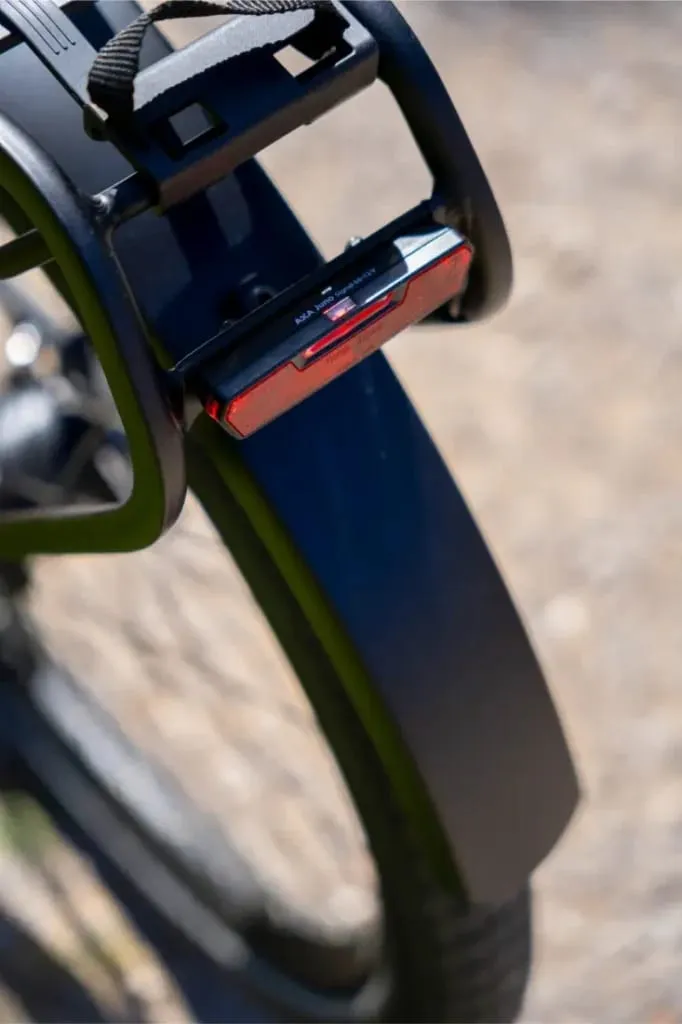 Primer plano del guardabarros trasero de una bicicleta con un reflector rojo y parte de un neumático de bicicleta visible, destacando el diseño lujo accesible visto en modelos como la Nevo5 de Riese & Müller.