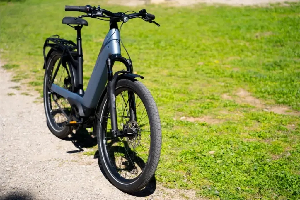 La bicicleta eléctrica Nevo5 de Riese & Müller, con tecnología CORE silenciosa, está aparcada en un camino de tierra junto a una zona de césped en un día soleado, ofreciendo un lujo accesible para tus aventuras al aire libre.