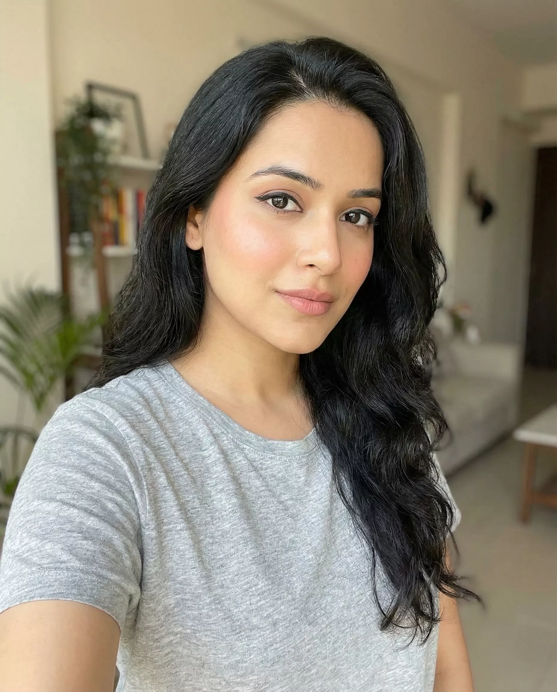 CozyVora customer review profile picture featuring a woman with long dark wavy hair wearing comfortable grey loungewear and minimal makeup in a modern home setting.